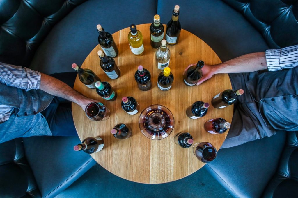 Two men sitting around an assortment of wine bottles.