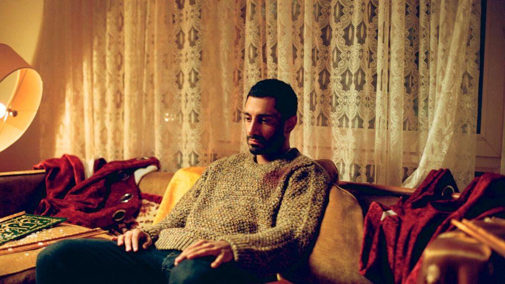 Riz Ahmed, Oscar winner, sitting on a couch.