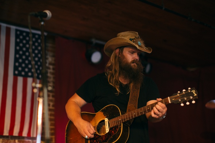 Chris Stapleton, who took home three Grammys, plays the guitar in front of an America flag.