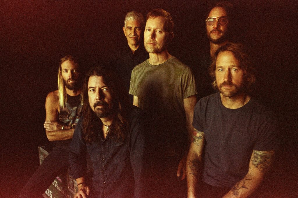 The Foo Fighters, who won three Grammys, sitting and standing in front of a black background.
