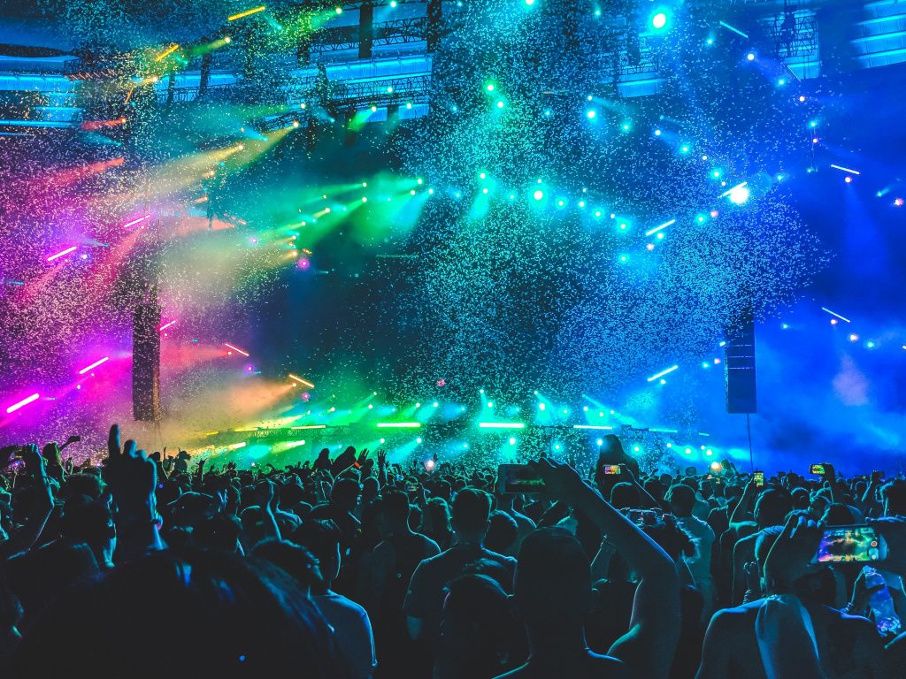 Colourful lights and confetti over a crowd at a music festival or concert.