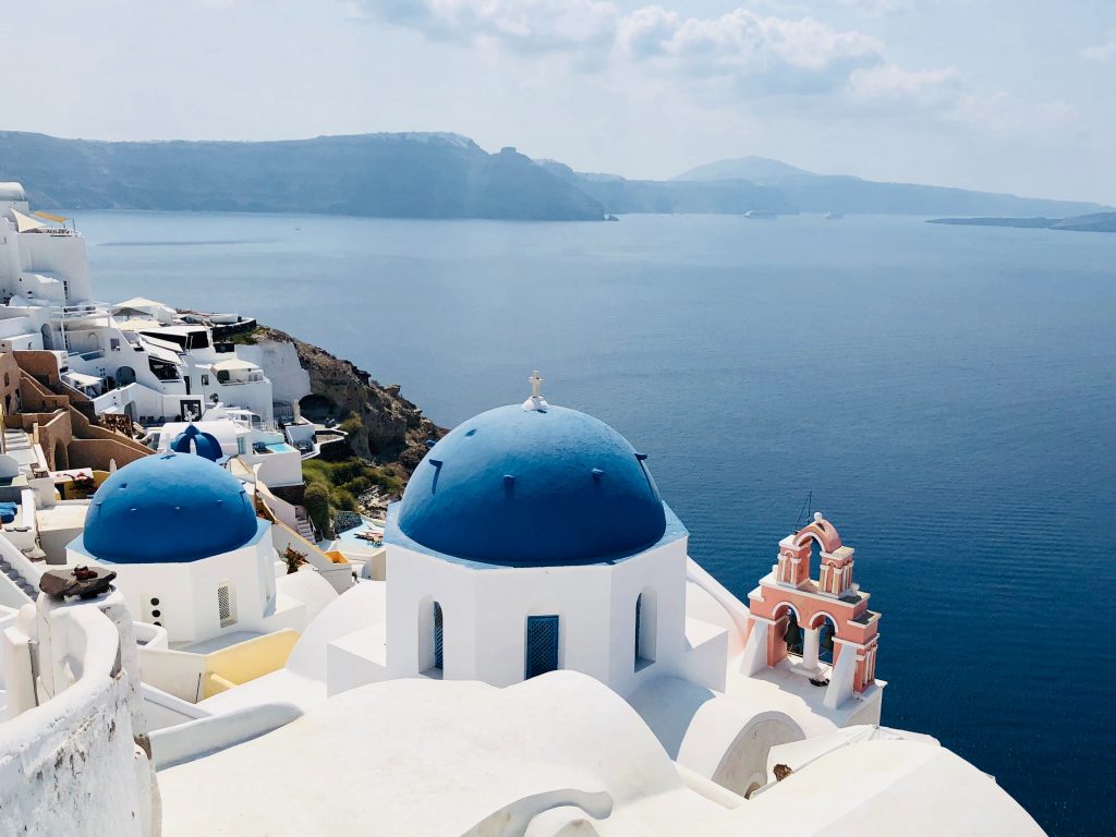 Oia, Santorini is a great place to catch the sunset. Two blue domed buildings overlooking the sea.