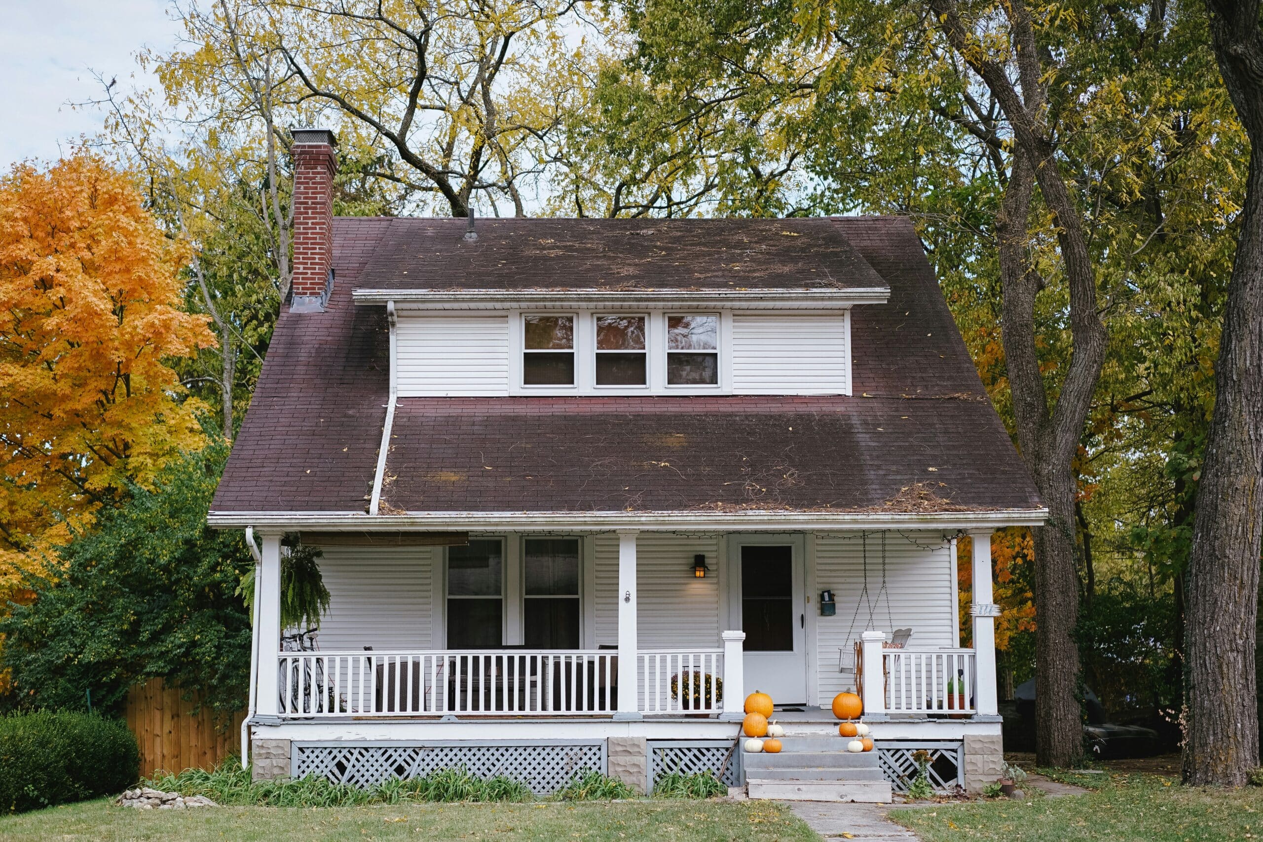 A white house with a porch and pumpkins on the steps, surrounded by autumn trees.