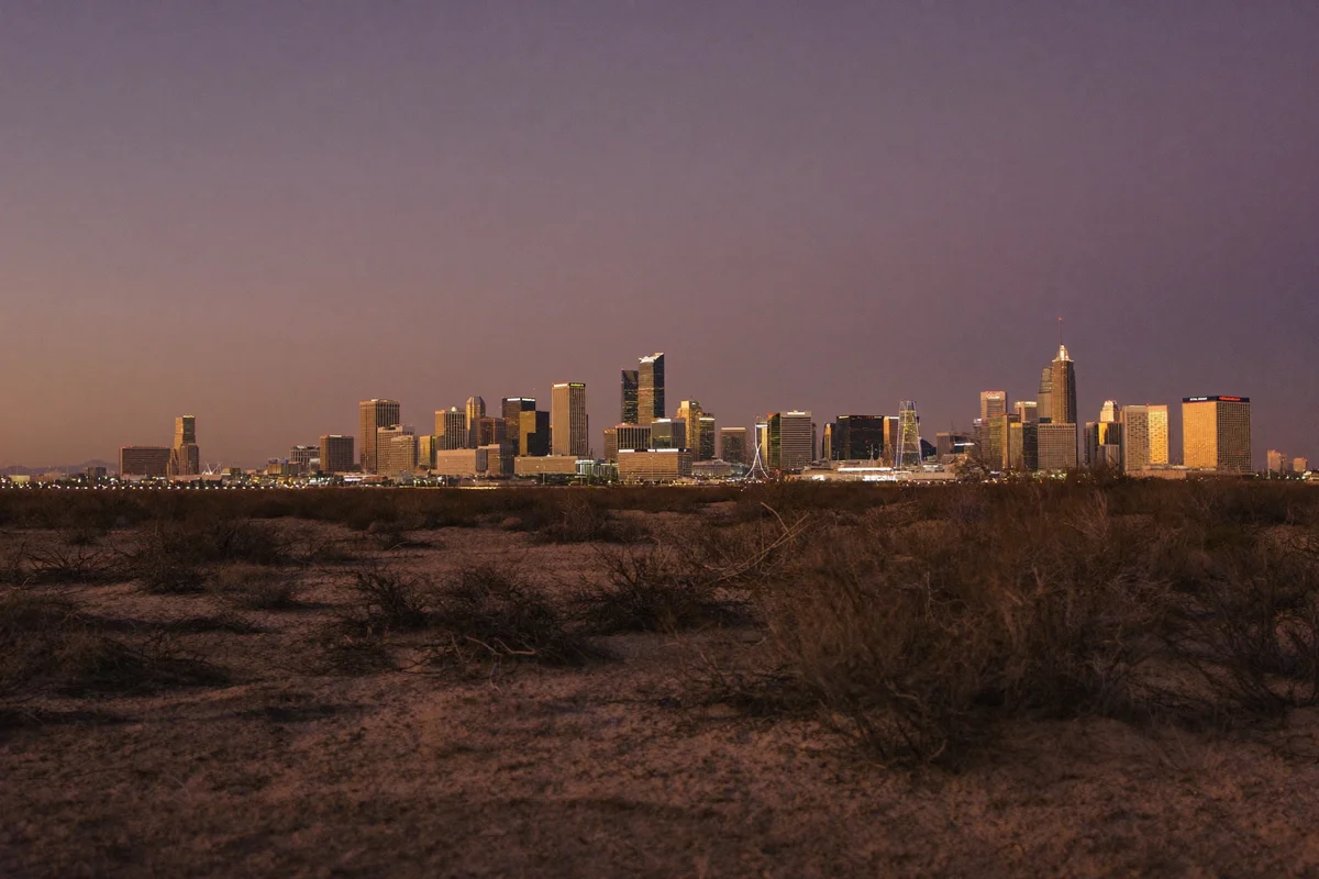 The Las Vegas skyline glowing at dusk, seen from scrubby desert ground outside the city
