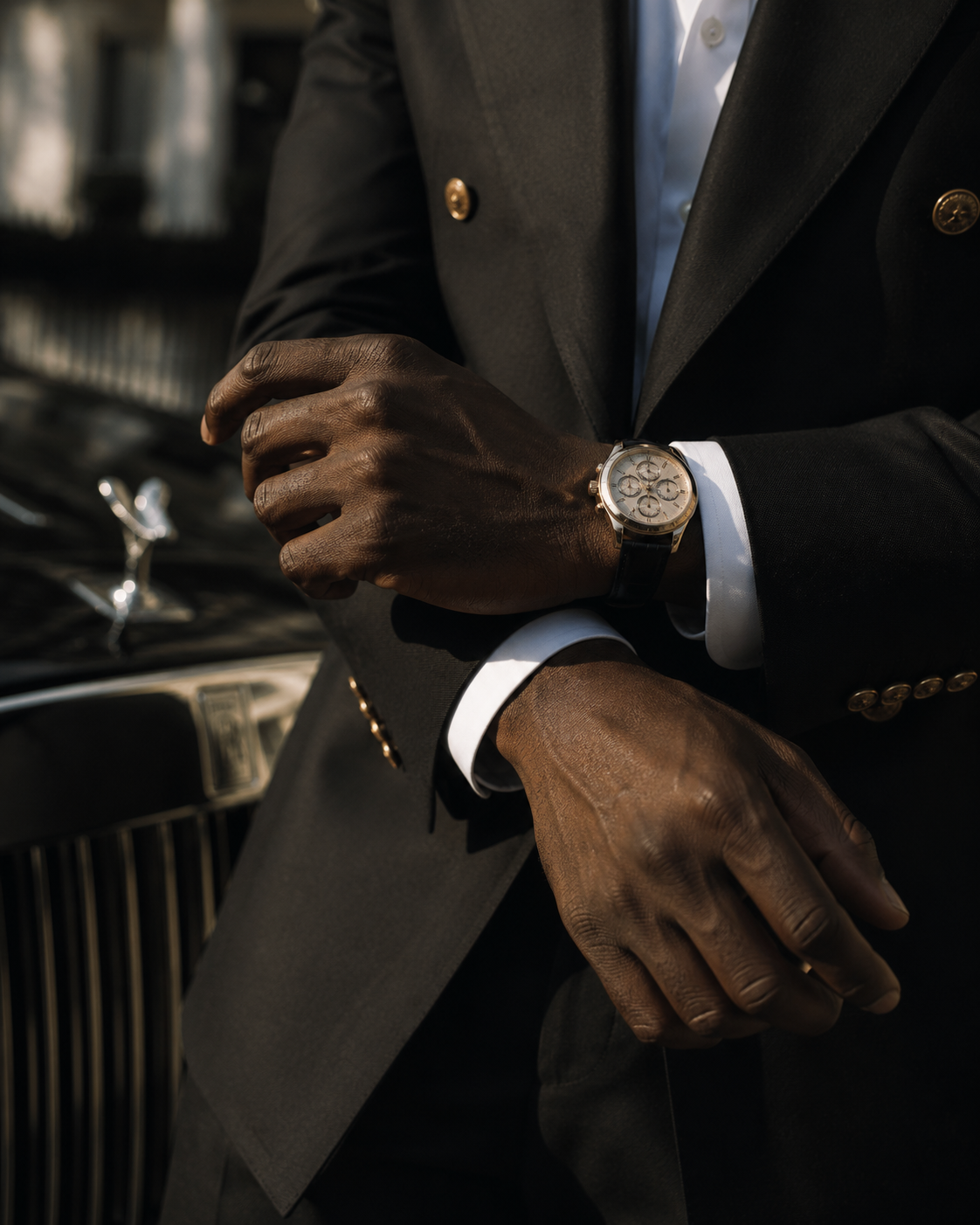 A close-up of a man in a dark suit adjusting his cufflinks and wristwatch beside a Rolls-Royce.